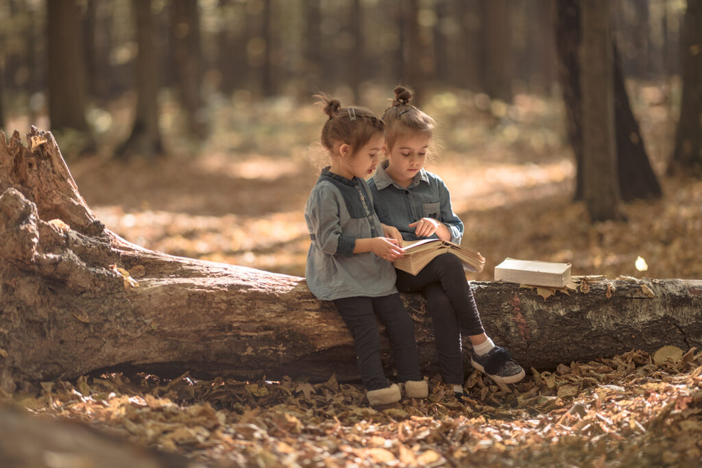 two little girls reading books in the woods.